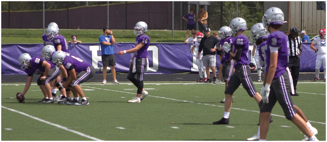 A group of people wearing purple football uniforms and helmets are positioned on a football field preparing for a play. Description generated by AI