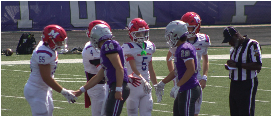 People in football uniforms are shaking hands on a field while a referee looks down at a device. Description generated by AI