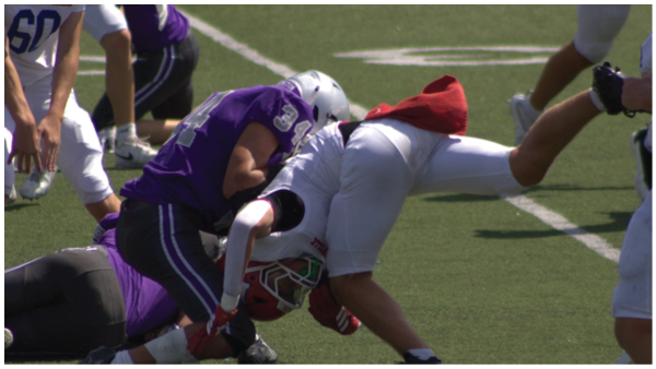 Two people in football gear are engaged in a tackle on a grassy field during a game. Description generated by AI