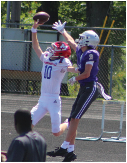 A person wearing a purple football uniform with the number one is running with a football while two people in white and red football uniforms are behind on a field with purple turf. Description generated by AI