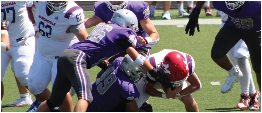 Several people in football uniforms are engaged in a tackle on a grassy field during a game. Description generated by AI