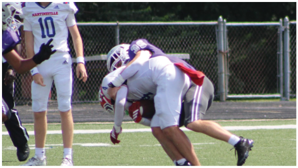 Two people wearing football gear are shown, one with a white jersey labeled MARTINSVILLE and the number 10, and the other wearing a helmet. Description generated by AI