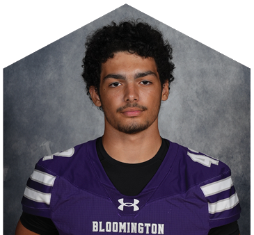 Person wearing a purple Bloomington sports jersey with white stripes on the shoulders and the Under Armour logo on the chest. Description generated by AI