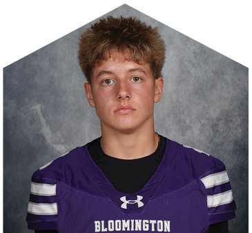 Person with short hair wearing a purple sports jersey with the word Bloomington on it against a gray textured background. Description generated by AI