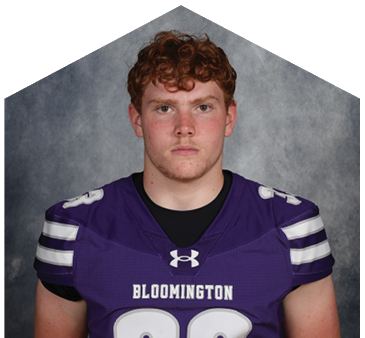 Person with curly hair wearing a purple Bloomington football jersey with the number 33 stands against a gray background. Description generated by AI