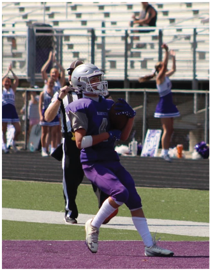 A person in a purple football uniform is catching a football in the end zone while cheerleaders in the background cheer with their arms raised. Description generated by AI