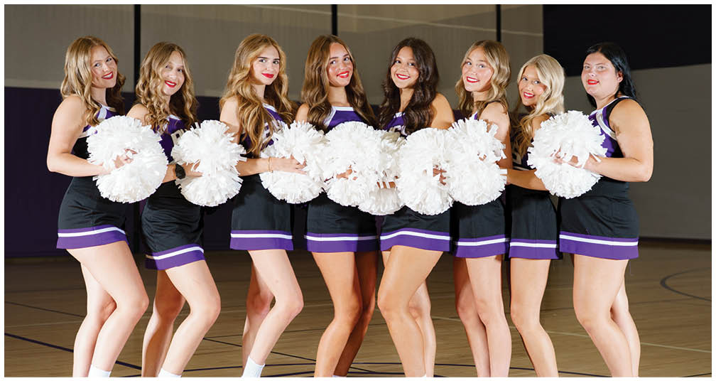 A group of people dressed in matching cheerleading uniforms with BHSS on the front are posing together holding purple and white pom-poms. Description generated by AI