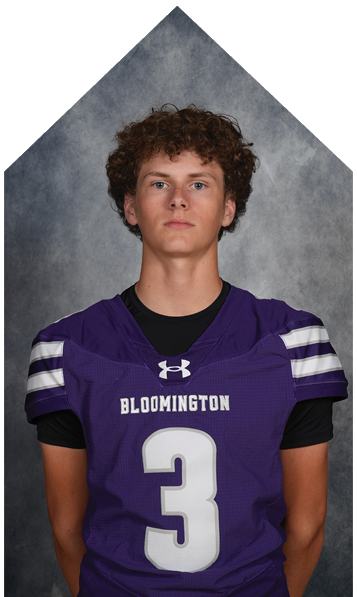 Person with curly hair wearing a purple sports jersey with the word Bloomington on the front against a gray background. Description generated by AI