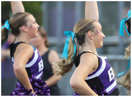 People wearing blue hair ribbons are holding up white pom-poms, likely participating in a cheerleading or sports event. Description generated by AI