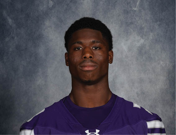 Person wearing a purple Bloomington football jersey with the number 73 standing against a dark textured background. Description generated by AI