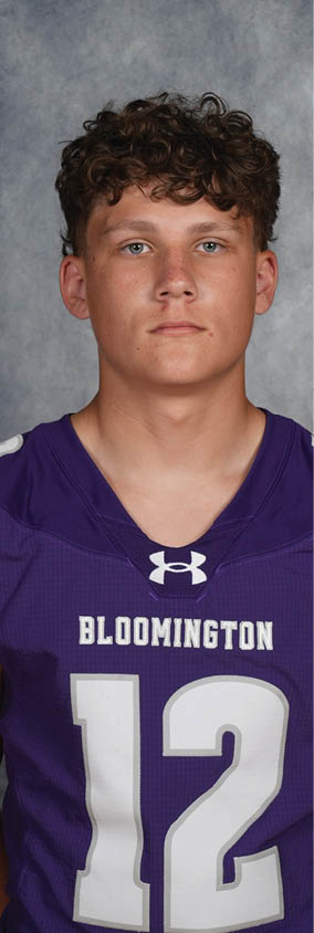 A person with curly hair wearing a purple Bloomington sports jersey with the number 12 stands against a gray textured background. Description generated by AI