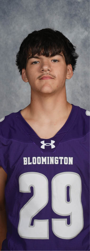 A person with short dark hair wearing a purple sports jersey with the number 29 and the word Bloomington on the front stands against a gray textured background. Description generated by AI