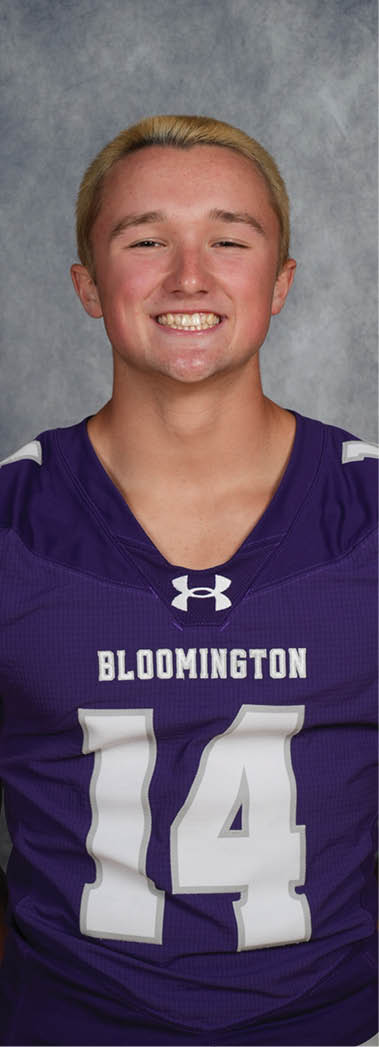 A person with short light hair is smiling and wearing a purple sports jersey with the word Bloomington and the number 14 on it. Description generated by AI