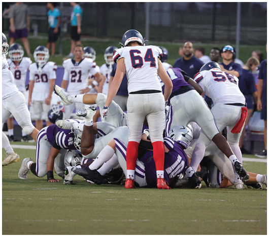 A group of football players in uniforms are piled on the ground during a game on a grassy field. Description generated by AI