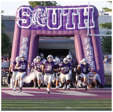 A group of people wearing purple and white football uniforms are running out from under a large inflatable archway that says “South Panthers" with a panther logo. Description generated by AI