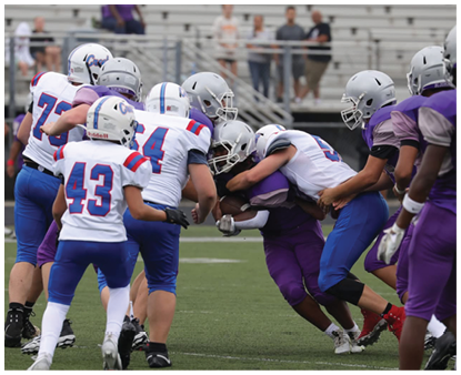 People wearing sports uniforms and cleats are positioned on a grassy field, appearing to prepare for a play or action. Description generated by AI