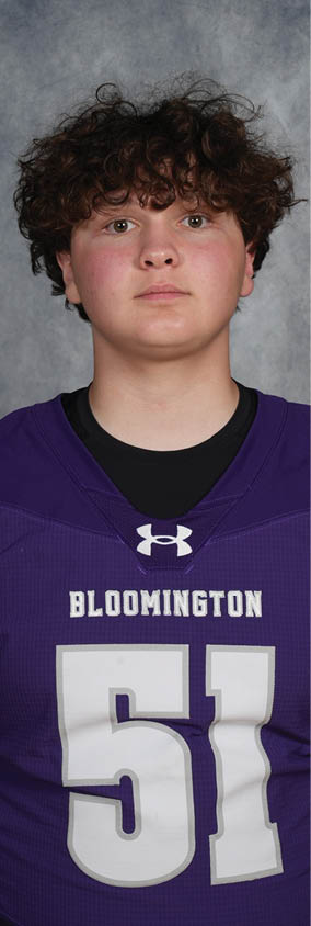 A person with curly hair wearing a purple Bloomington sports jersey with the number 51 stands against a gray textured background. Description generated by AI