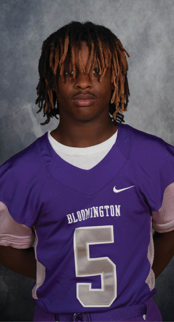 Person with medium-length dreadlocks wearing a purple sports jersey with the word Bloomington and a white Nike logo. Description generated by AI