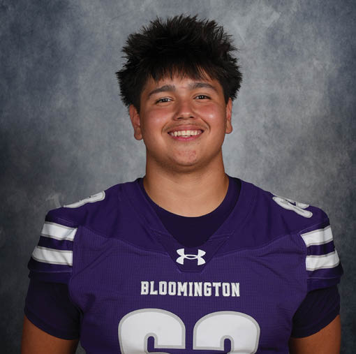 Person with spiky hair wearing a purple sports jersey with the word Bloomington smiling against a gray textured background. Description generated by AI