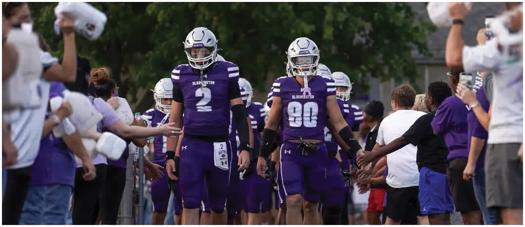 People in purple football uniforms walk down a path lined with others reaching out to high-five them. Description generated by AI