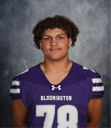 A person with curly hair wearing a purple Bloomington sports jersey with the number 78 stands against a gray mottled background. Description generated by AI