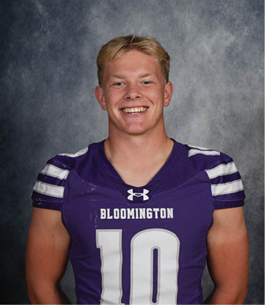 A person with short light hair is smiling and wearing a purple Bloomington football jersey with the number 10. Description generated by AI