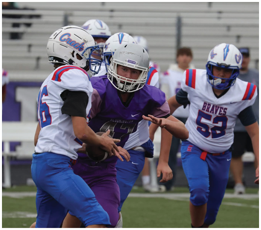 Two people in football uniforms are engaged in a play with one holding a football while the other appears to be preparing to receive or block. Description generated by AI