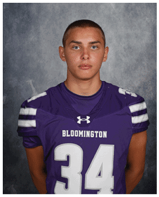 A person wearing a purple Bloomington football jersey with the number 34 stands against a gray textured background. Description generated by AI