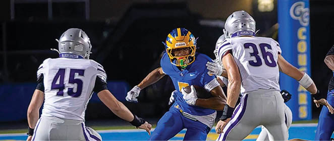 Three people wearing football helmets and uniforms are positioned closely together on a field with a dark background. Description generated by AI