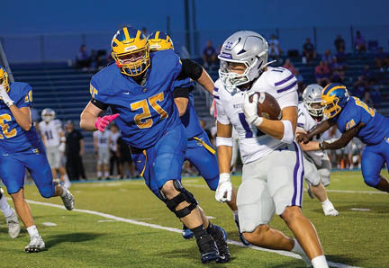 A person in a white football uniform is running with the ball while several people in blue and yellow football uniforms chase them on a field. Description generated by AI