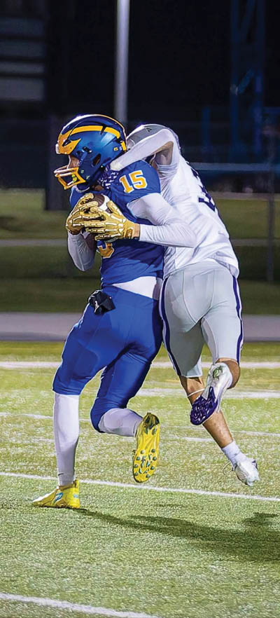 A person wearing a blue and yellow football uniform with the number 15 is running on a field while holding a football. Description generated by AI
