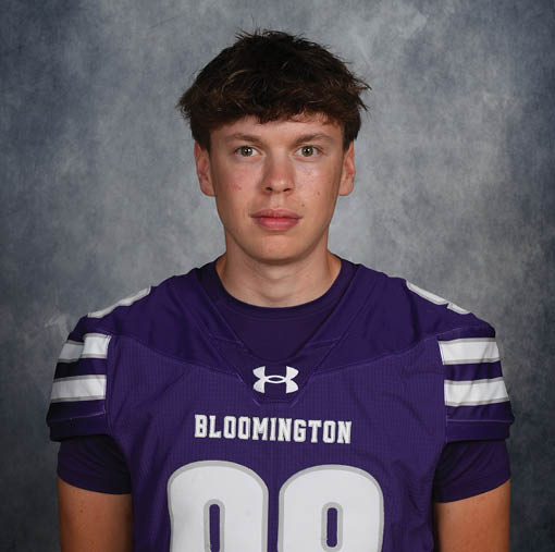 A person with short, tousled hair is wearing a purple sports jersey with white stripes on the shoulders and the word Bloomington printed on the front. Description generated by AI