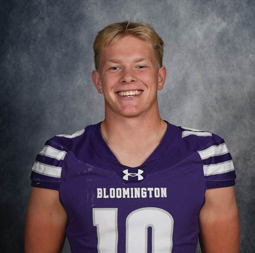A person with short light hair is smiling and wearing a purple sports jersey with the word Bloomington and the number 10 on it against a gray mottled background. Description generated by AI
