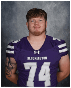 Person with short hair wearing a purple football jersey with the number 74 and the word Bloomington on the front, standing against a gray textured background. Description generated by AI