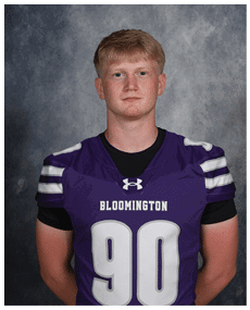 A person with short hair wearing a purple Bloomington football jersey with the number 90 stands against a gray textured background. Description generated by AI