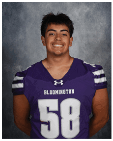A person with short dark hair is smiling and wearing a purple sports jersey with the number 58 and the word Bloomington on the front. Description generated by AI