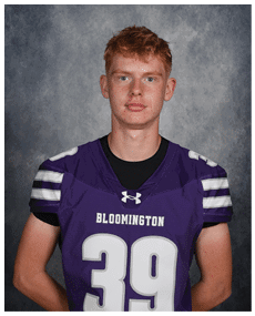 A person with short hair wearing a purple Bloomington sports jersey with the number 39 stands against a gray textured background. Description generated by AI
