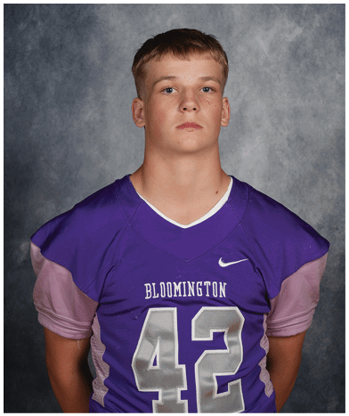 A person wearing a purple Bloomington football jersey with the number 42 stands against a gray mottled background. Description generated by AI