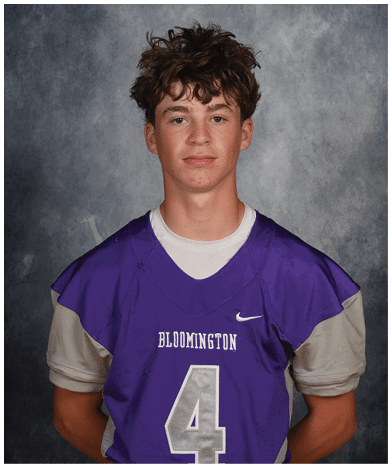 A person with curly hair wearing a purple sports jersey with the word Bloomington and the number 4 stands against a gray textured background. Description generated by AI