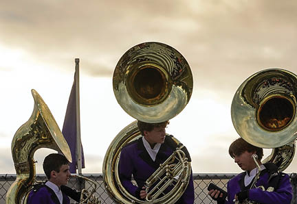 Three people in matching purple band uniforms are playing large brass sousaphones outdoors against a cloudy sky. Description generated by AI