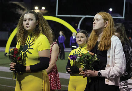 Several people with varied hairstyles stand outdoors at night near a sports field with a goalpost visible in the background. Description generated by AI