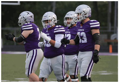 People wearing purple and gray football uniforms and helmets are standing on a football field. Description generated by AI