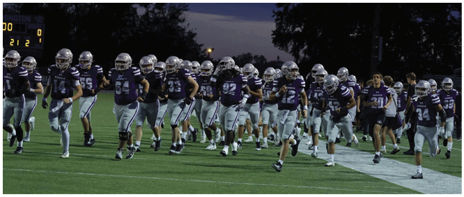 A group of people wearing football uniforms and helmets are running onto a field at dusk. Description generated by AI