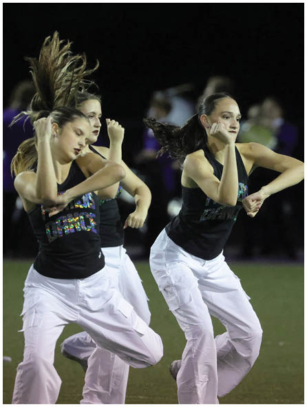 Three people wearing black tops and white pants are energetically dancing on a field at night. Description generated by AI