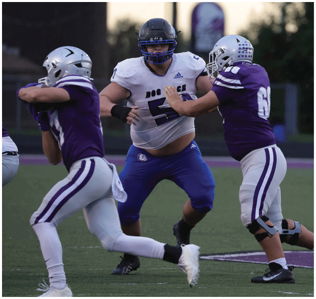 Three people wearing football uniforms and helmets are engaged in a play on a football field during a game. Description generated by AI