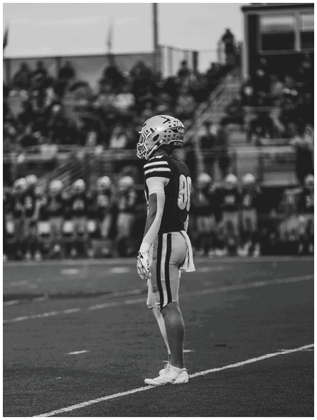 A person wearing a football helmet and uniform is standing on the right side of the image with a blurred crowd in the background. Description generated by AI