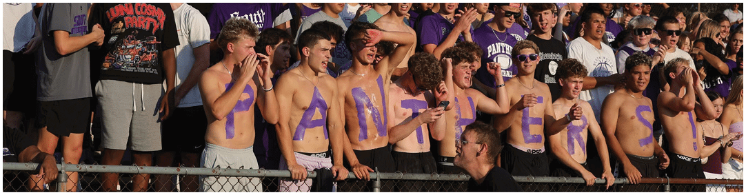 People wearing purple football uniforms and helmets are standing together in a tunnel or hallway. Description generated by AI