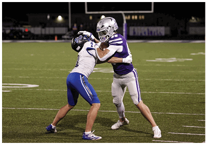 Two people in football uniforms are engaged in a physical struggle on a lit football field at night. Description generated by AI