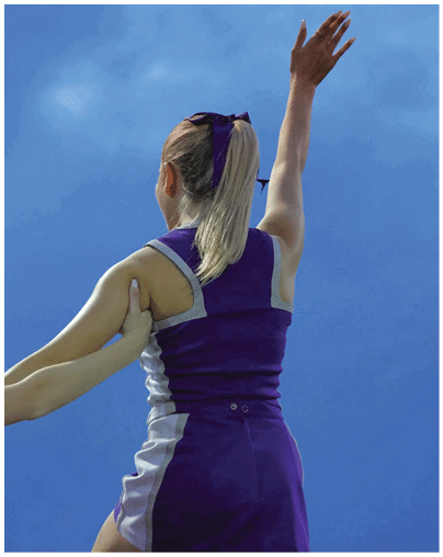 Two people in purple and white cheerleading uniforms perform a stunt outdoors against a blue sky. Description generated by AI