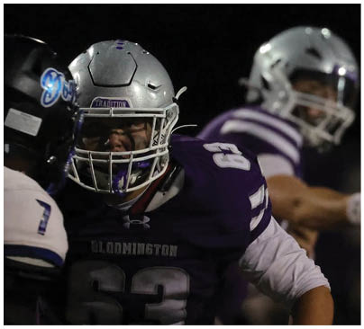 People wearing football helmets and uniforms are engaged in a game under a dark sky. Description generated by AI